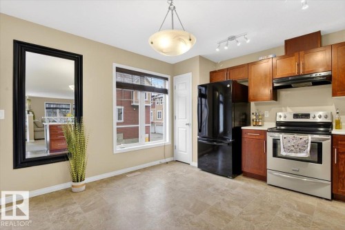 The kitchen features wood cabinetry, stainless steel appliances including a refrigerator and range, and light-colored tile flooring - 1637 Towne Centre Boulevard, Edmonton, AB - Indoor Photo Showing Kitchen