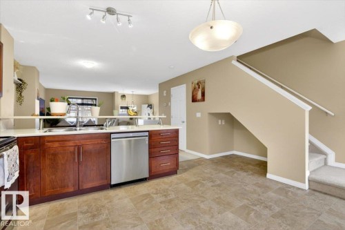 Kitchen featuring a stainless steel dishwasher, an integrated sink, and wood cabinetry, with tiled flooring extending into the hallway - 1637 Towne Centre Boulevard, Edmonton, AB - Indoor Photo Showing Kitchen With Double Sink
