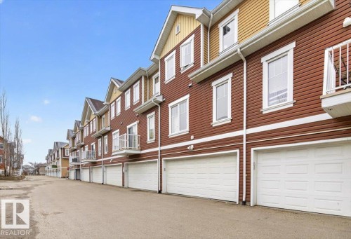 The property features a row of multi-story townhomes with red and yellow siding, individual white garage doors, and white-framed windows - 1637 Towne Centre Boulevard, Edmonton, AB - Outdoor With Exterior