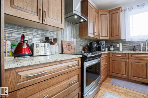 The kitchen features wood cabinetry, granite countertops, a tile backsplash, and a stainless steel range with an overhead exhaust hood - 18 Enchanted Way, St. Albert, AB 
