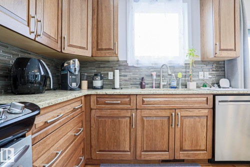 Kitchen featuring wood cabinetry, a granite countertop, a tiled backsplash, and a stainless steel dishwasher - 18 Enchanted Way, St. Albert, AB 