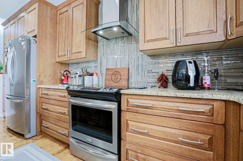 Kitchen featuring wooden cabinetry, a stainless steel refrigerator, a stainless steel range oven, and a tiled backsplash - 18 Enchanted Way, St. Albert, AB 