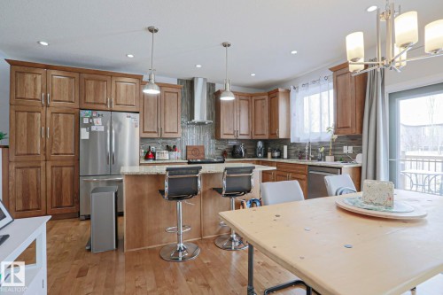 The kitchen features wood cabinetry, stainless steel appliances, a breakfast bar, and a tile backsplash - 18 Enchanted Way, St. Albert, AB 