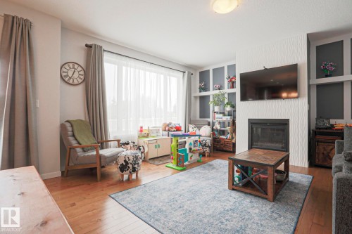 This living space features hardwood floors, a large window providing natural light, and a fireplace with a textured surround - 18 Enchanted Way, St. Albert, AB 