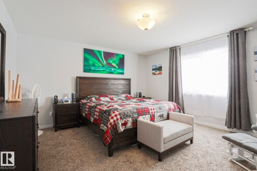 Bedroom featuring light-colored walls, carpeted flooring, and a window with curtains and a sheer blind - 18 Enchanted Way, St. Albert, AB 