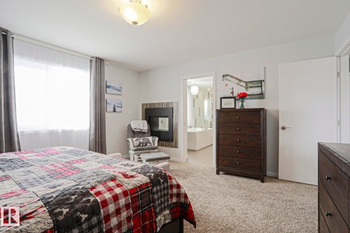 This bedroom features light-colored carpet, a window with curtains, and a fireplace with a wood surround - 18 Enchanted Way, St. Albert, AB 