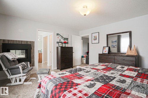 The bedroom features a built-in fireplace with a paneled surround, light gray carpet, and a ceiling-mounted light fixture - 18 Enchanted Way, St. Albert, AB 