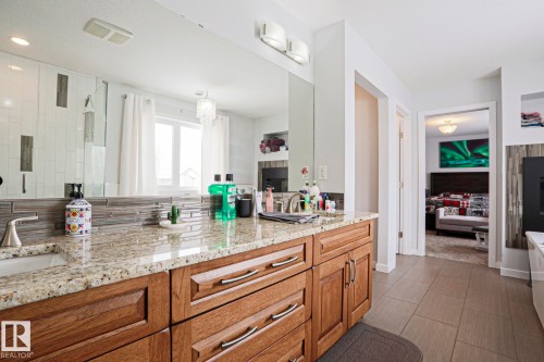 The bathroom features a double vanity with a granite countertop, wooden cabinetry, and tile flooring - 18 Enchanted Way, St. Albert, AB 