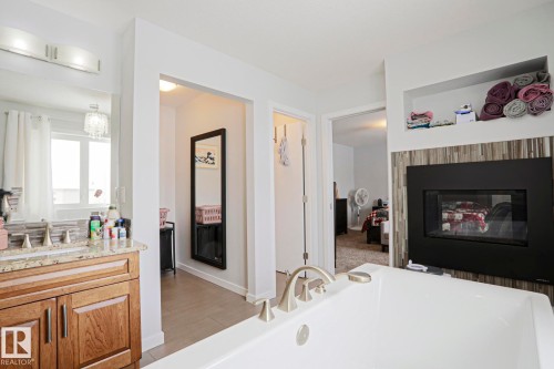 Well-appointed bathroom featuring a white soaking tub, a fireplace with a tiled surround, and a vanity with a granite countertop and wooden cabinetry - 18 Enchanted Way, St. Albert, AB 