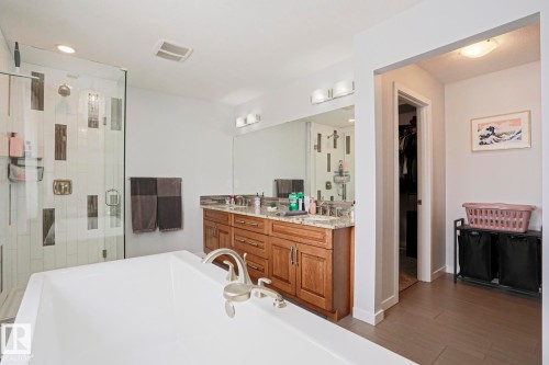 Well-appointed bathroom featuring a soaking tub, a walk-in shower with a glass enclosure and tiled walls, a vanity with a granite countertop and dual sinks, and light-colored flooring - 18 Enchanted Way, St. Albert, AB 