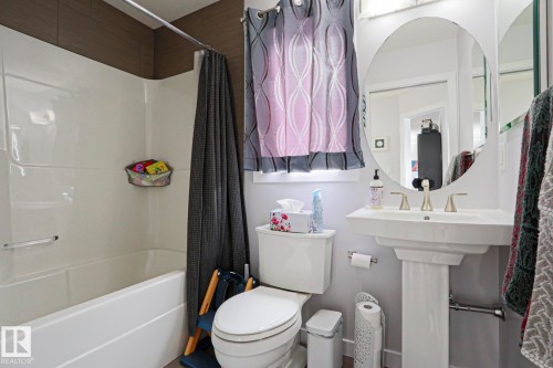 The bathroom features a white pedestal sink with a contemporary faucet, a toilet, and a bathtub with a shower - 18 Enchanted Way, St. Albert, AB 