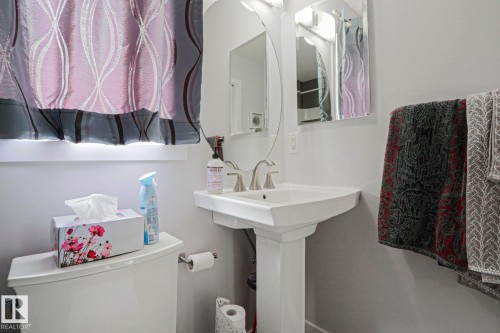 Bathroom featuring a white pedestal sink with a brushed nickel faucet, a mirror with an oval frame, and light gray walls - 18 Enchanted Way, St. Albert, AB 