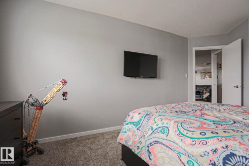 The room features neutral gray walls, carpeting, and a television mounted on the wall - 18 Enchanted Way, St. Albert, AB 