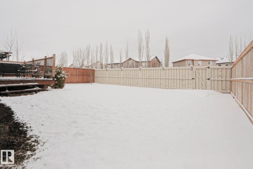 The property features a spacious backyard with a wooden deck, a light-colored privacy fence, and a wooden gate - 18 Enchanted Way, St. Albert, AB 