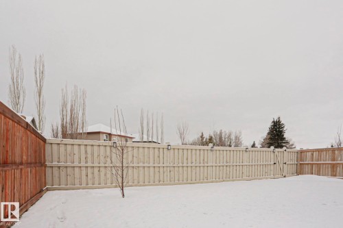 The property features a fenced yard with a gate, a light-colored wooden fence, and a bare tree - 18 Enchanted Way, St. Albert, AB 