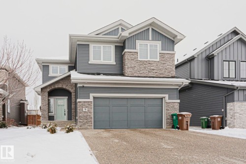 The property features a two-story exterior with grey siding and stone accents, a two-car garage, and a light-colored front door - 18 Enchanted Way, St. Albert, AB 
