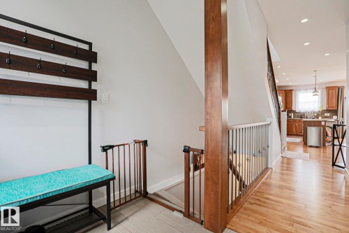 The property features hardwood flooring in the main hallway and recessed lighting, leading towards the kitchen with wood cabinetry and stainless steel appliances - 18 Enchanted Way, St. Albert, AB 