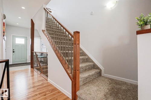 The entryway features hardwood flooring, a staircase with carpeting and wooden handrails, and a light-colored front door with a window - 18 Enchanted Way, St. Albert, AB 