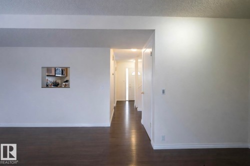 This interior space features dark wood flooring, white walls, and a pass-through window to the kitchen - 1728 37 Street, Edmonton, AB - Indoor Photo Showing Other Room