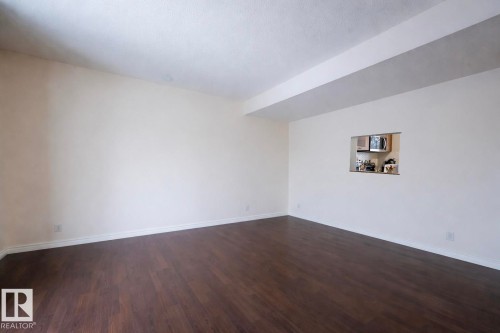 Spacious room featuring dark wood flooring, light-colored walls, and a pass-through window looking into a kitchen area - 1728 37 Street, Edmonton, AB - Indoor Photo Showing Other Room