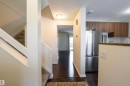 The property features dark wood flooring, a carpeted staircase with white railings, and a kitchen area with wood cabinets, a stainless steel refrigerator, and a white tile backsplash - 1728 37 Street, Edmonton, AB  - Indoor 
