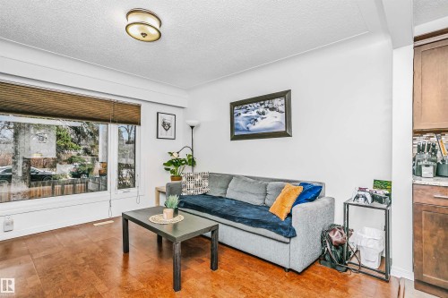 Living area featuring warm-toned hardwood floors, a large window with blinds, and a ceiling-mounted light fixture - 6524 112 Street, Edmonton, AB - Indoor Photo Showing Living Room