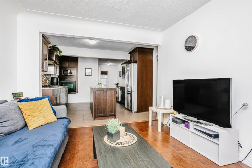 The property features a bright living area with hardwood flooring, offering an open view into the kitchen, which is equipped with dark wood cabinetry, a central island, and stainless steel appliances - 6524 112 Street, Edmonton, AB - Indoor Photo Showing Living Room
