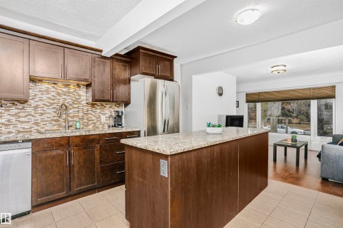 Well-appointed kitchen featuring dark wood cabinetry, a mosaic tile backsplash, granite countertops, and stainless steel appliances - 6524 112 Street, Edmonton, AB - Indoor Photo Showing Kitchen With Upgraded Kitchen