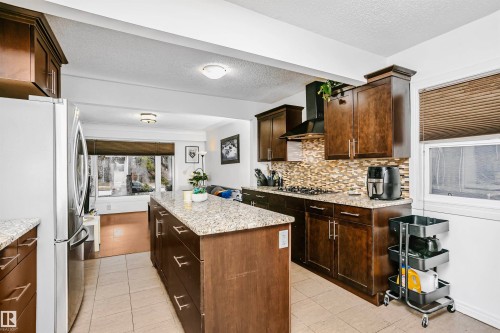 The kitchen features a central island with a granite countertop, rich wood cabinetry, and a patterned tile backsplash - 6524 112 Street, Edmonton, AB - Indoor Photo Showing Kitchen With Upgraded Kitchen