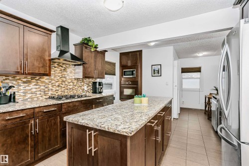 The kitchen features rich wood cabinetry, a granite island and countertops, a tiled backsplash, and stainless steel appliances - 6524 112 Street, Edmonton, AB - Indoor Photo Showing Kitchen With Upgraded Kitchen