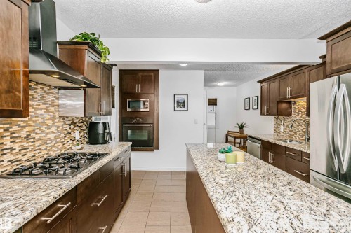 The kitchen features extensive granite countertops, dark wood cabinetry, and a mosaic tile backsplash - 6524 112 Street, Edmonton, AB - Indoor Photo Showing Kitchen With Upgraded Kitchen