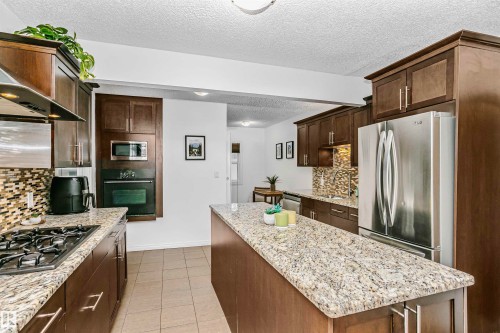 The kitchen features granite countertops, dark wood cabinetry, stainless steel appliances, and a tiled backsplash - 6524 112 Street, Edmonton, AB - Indoor Photo Showing Kitchen With Upgraded Kitchen