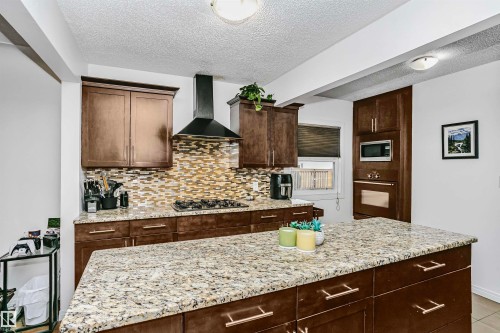 The kitchen features dark wood cabinetry, granite countertops, a patterned tile backsplash, and stainless steel appliances including a built-in microwave and oven - 6524 112 Street, Edmonton, AB - Indoor Photo Showing Kitchen