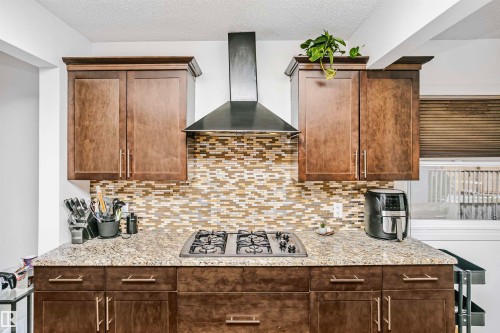 The kitchen features rich wood cabinetry, a mosaic tile backsplash, a built-in cooktop, and a matching range hood - 6524 112 Street, Edmonton, AB - Indoor Photo Showing Kitchen