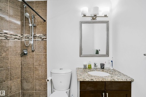 Bathroom featuring a tiled shower with a decorative accent band, a vanity with a granite countertop, and a framed mirror - 6524 112 Street, Edmonton, AB - Indoor Photo Showing Bathroom