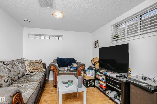 This living area features a window with blinds, a glass block window, and light-toned flooring - 6524 112 Street, Edmonton, AB - Indoor