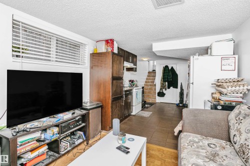 This living area features a window with blinds, tile flooring, and a portion of a kitchen with dark wood cabinets - 6524 112 Street, Edmonton, AB - Indoor Photo Showing Living Room