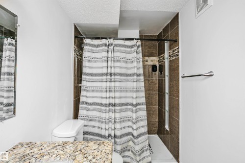 The bathroom features a tiled shower with decorative accent tiling, a mirror, and a vanity with a granite countertop - 6524 112 Street, Edmonton, AB - Indoor Photo Showing Bathroom