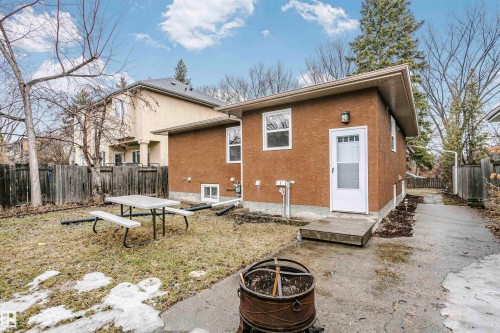 The property features a brown stucco exterior, a white door with a window, and a concrete pathway leading to a fenced yard - 6524 112 Street, Edmonton, AB - Outdoor