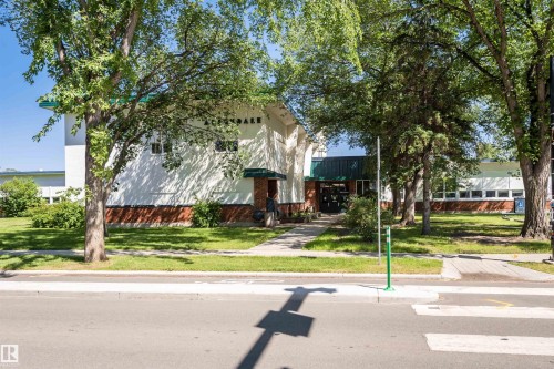 The property features a white exterior with a brick base, a green roofline, and a well-maintained lawn with mature trees - 6524 112 Street, Edmonton, AB - Outdoor