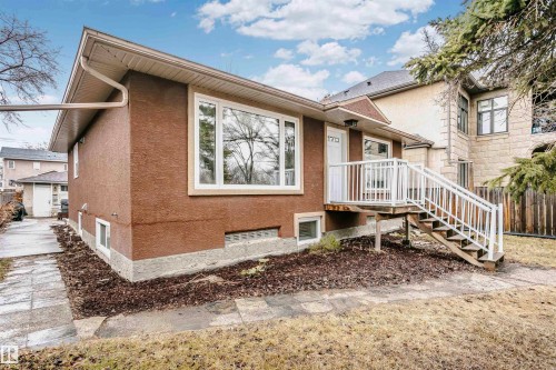 The property features a stucco exterior with a large front window, a white main entry door, and an exterior staircase with white railings leading to the entrance - 6524 112 Street, Edmonton, AB - Outdoor With Exterior