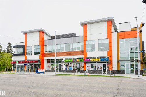 The property features a modern facade with white, orange, and dark grey paneling, large storefront windows, and a prominent position along a paved road - 6524 112 Street, Edmonton, AB - Outdoor