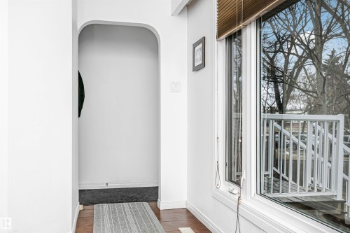 This space features a large window with horizontal blinds, offering views of mature trees and a white railing - 6524 112 Street, Edmonton, AB -  With Exterior