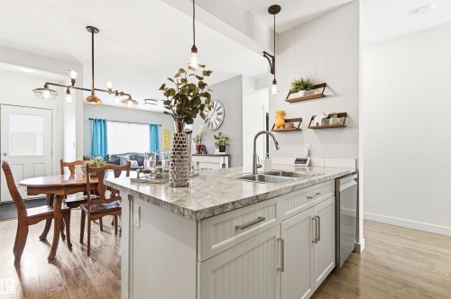 The kitchen features a center island with a double sink, stainless steel faucet, and light-colored countertops - 678 Secord Boulevard, Edmonton, AB - Indoor