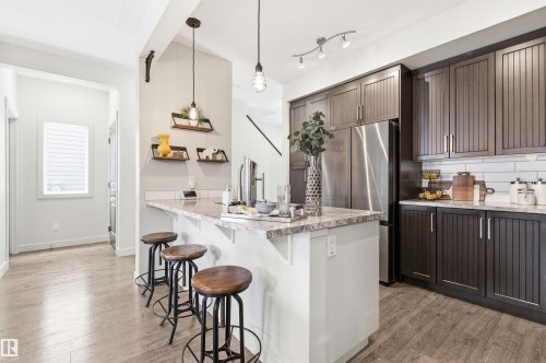 The kitchen features dark wood cabinetry, stainless steel appliances, and a central island with a light-colored countertop - 678 Secord Boulevard, Edmonton, AB - Indoor Photo Showing Kitchen With Upgraded Kitchen