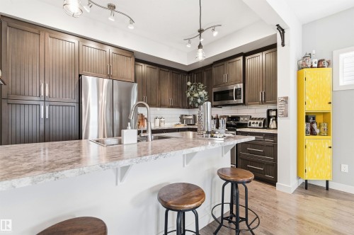 The kitchen features extensive dark wood cabinetry, stainless steel appliances, and a central island with a sink and ample countertop space - 678 Secord Boulevard, Edmonton, AB - Indoor Photo Showing Kitchen With Upgraded Kitchen