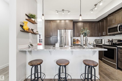 The kitchen features dark wood cabinetry, stainless steel appliances, and an island with a light-colored countertop - 678 Secord Boulevard, Edmonton, AB - Indoor Photo Showing Kitchen With Double Sink With Upgraded Kitchen