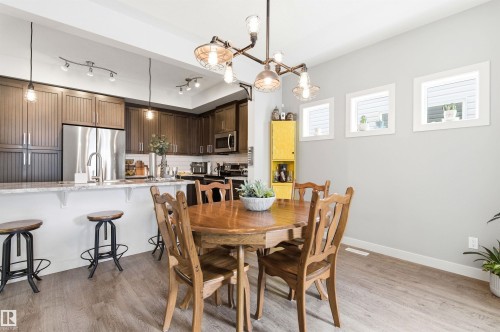 The kitchen features dark wood cabinetry, stainless steel appliances, and a light-colored countertop with a breakfast bar - 678 Secord Boulevard, Edmonton, AB - Indoor Photo Showing Dining Room