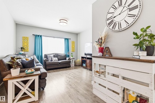 The property features a living area with light-toned flooring, light-colored walls, and a window with blue curtains providing natural illumination - 678 Secord Boulevard, Edmonton, AB - Indoor Photo Showing Living Room