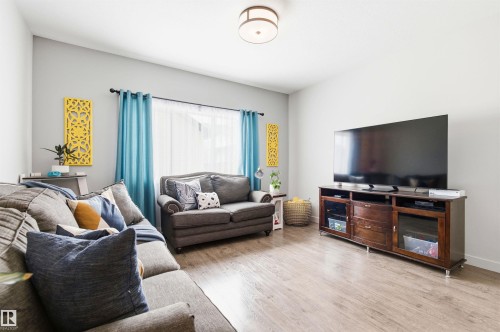 Living area featuring light-toned flooring, light gray walls, and a window with sheer white blinds and blue curtains - 678 Secord Boulevard, Edmonton, AB - Indoor Photo Showing Living Room